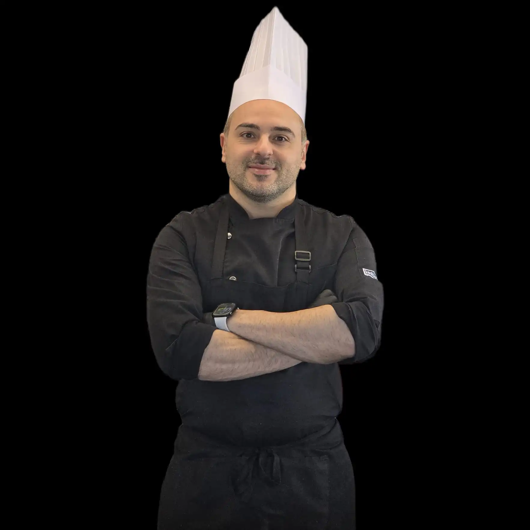 Chef wearing a black uniform and white hat with arms crossed.